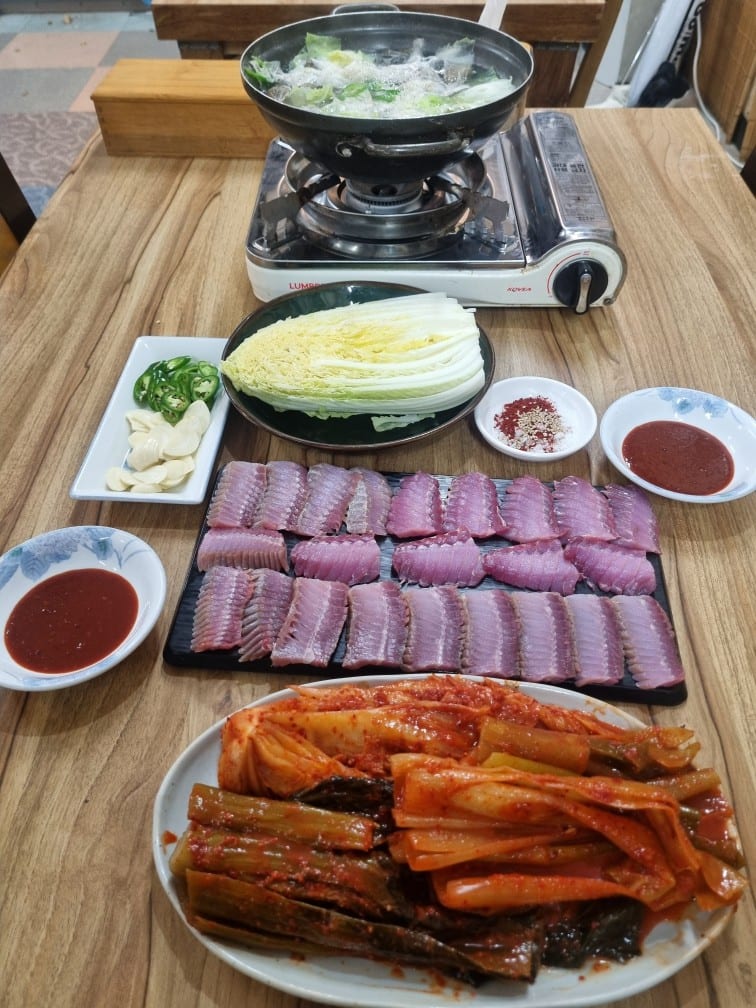 검은 접시에 가지런히 놓인 홍어사시미와 김치, 배추, 초장, 버너 위 홍어 지리