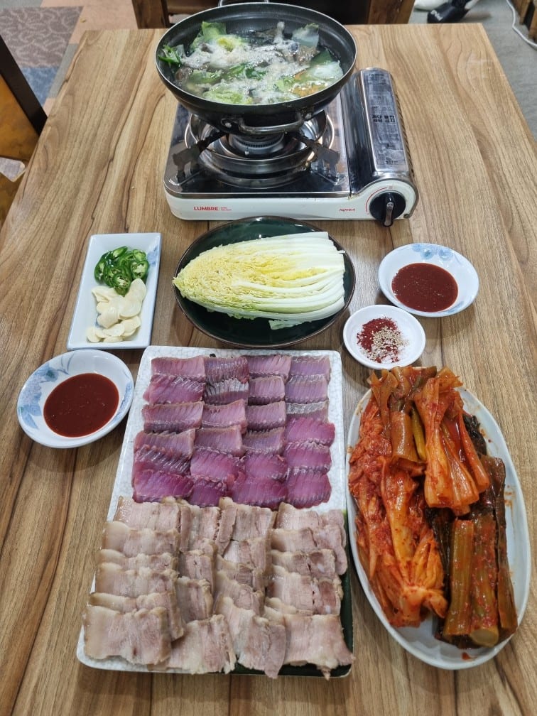 홍어삼합 상차림. 홍어와 수육을 한 접시에 담고 묵은지·갓김치, 배추, 마늘·고추, 초장, 버너 위 홍어 지리가 함께 놓였다
